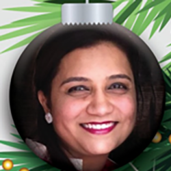 A womans smiling face is featured inside a Christmas tree ornament with green pine needles and gold accents in the background.