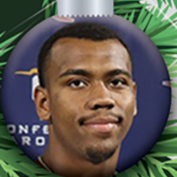 A Christmas tree ornament shaped like a bauble features a young man with short hair and a faint mustache, set against a blue background with green pine needles around the ornament.