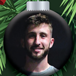 A Christmas tree ornament featuring a photo of a smiling man with short brown hair and a beard, surrounded by green pine needles.