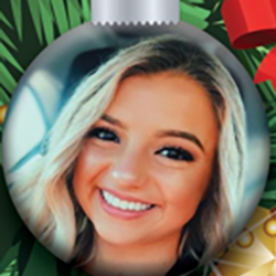 A close-up photo of a young woman with blonde hair, smiling brightly, is featured inside a round Christmas ornament, surrounded by green pine branches and red decorations.