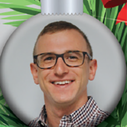 A smiling person with short hair and glasses is pictured inside a silver Christmas ornament, with green foliage and red decorations in the background.