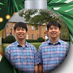 Two young men wearing matching plaid shirts stand side by side, smiling, with a brick building and trees in the background, all framed within a round holiday ornament graphic.