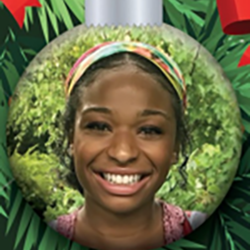A smiling woman with a colorful headband is pictured inside a round ornament with a leafy green background and red ribbons, resembling a Christmas decoration.