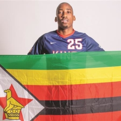 A person wearing a dark blue sports jersey with the number 25 holds up the Zimbabwean flag, which features green, gold, red, and black stripes with a white triangle and a red star with a yellow bird.