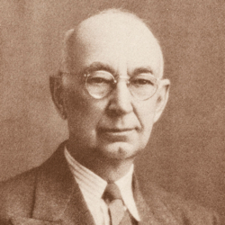 Sepia-toned portrait of an older man with glasses, a bald head, and wearing a suit, collared shirt, and tie, facing forward with a neutral expression.