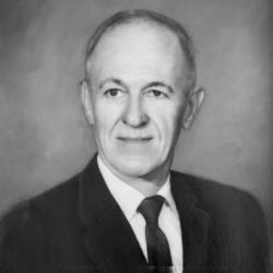 Black and white portrait of an older man wearing a suit and tie, with short hair and a calm expression, looking slightly to the side against a plain background.