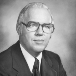 Black-and-white portrait of an older man with glasses, short white hair, and a suit and tie, looking slightly off-camera against a neutral background.