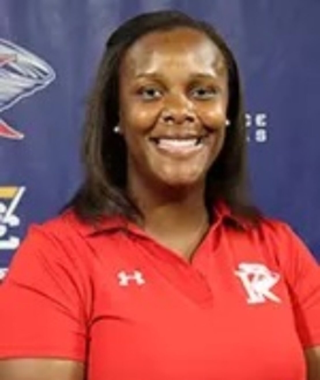 A woman wearing a red short-sleeve polo shirt with a white R logo smiles in front of a blue backdrop featuring athletic logos.
