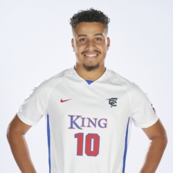Smiling soccer player wearing a white jersey with blue and red accents, the number 10, and the word KING on the front. He stands with his hands on his hips against a plain light background.
