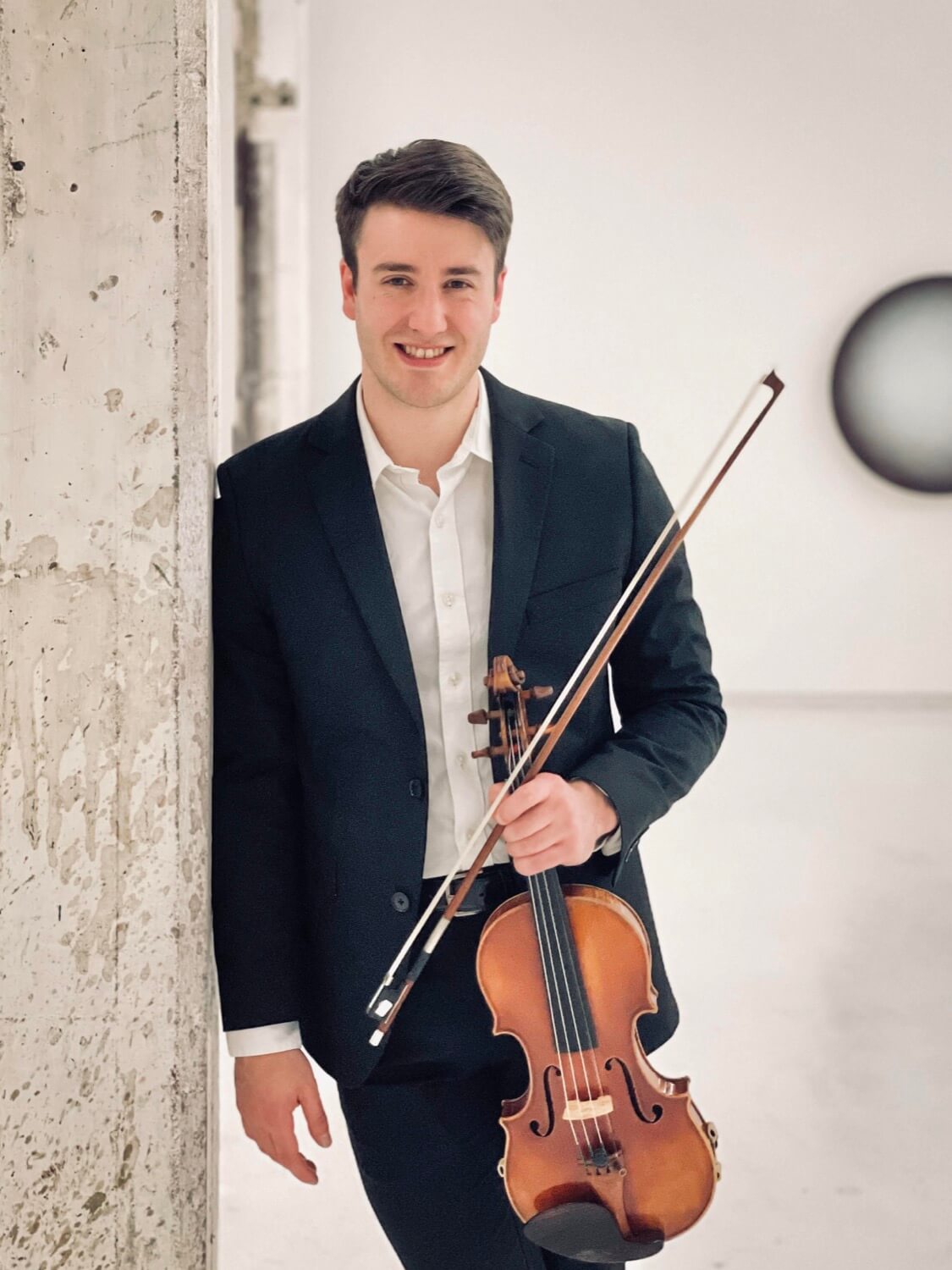 Tobias Elser smiling with his violin and bow in hand